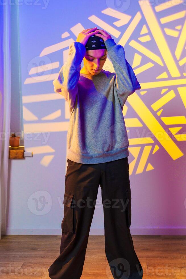 A young person stands with their hands on their head, looking down, in front of a wall with a projected pattern photo