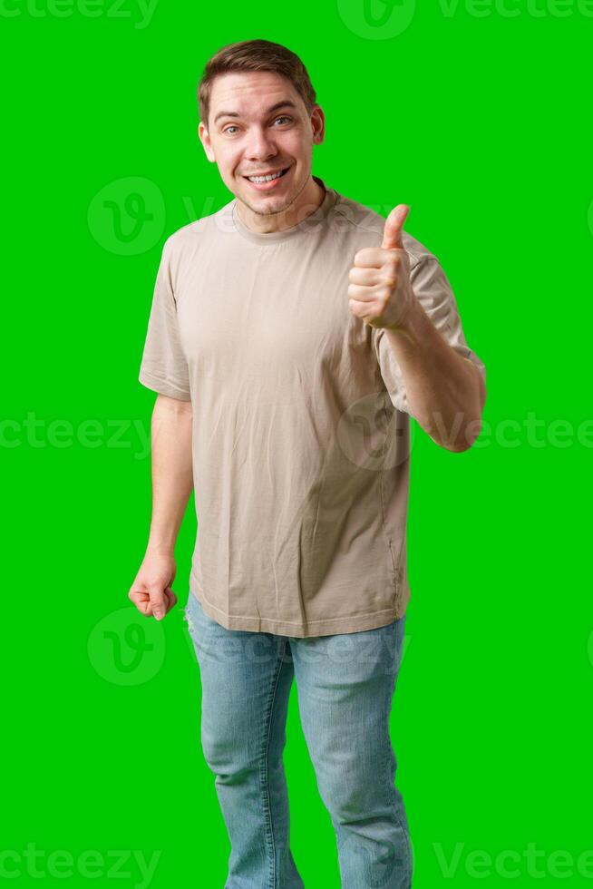 A man in a beige shirt gives a thumbs up while standing against a green background photo