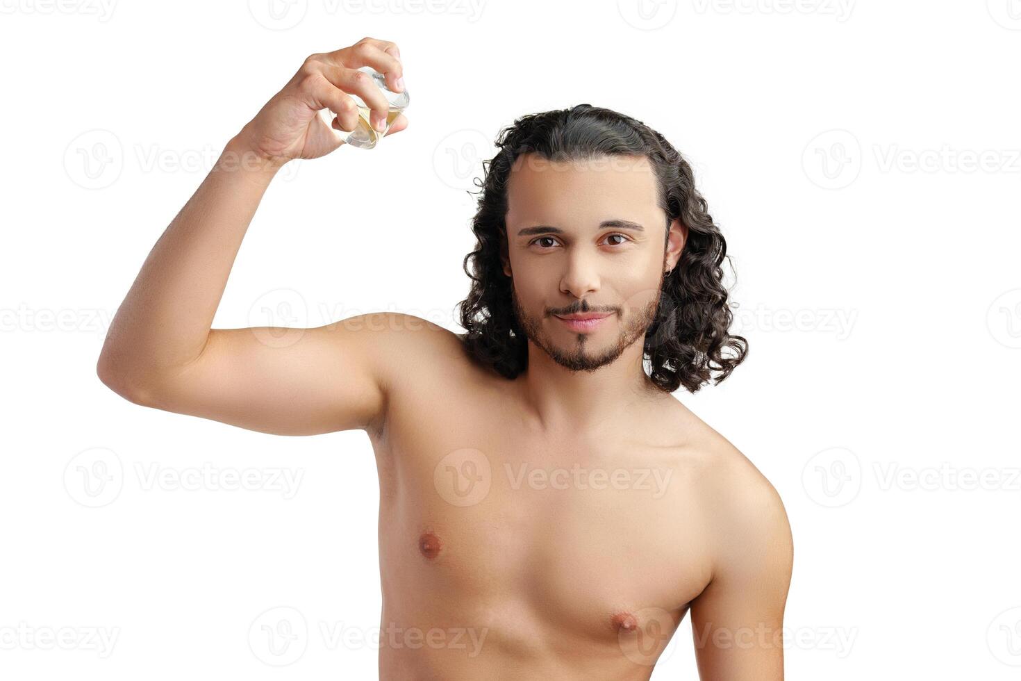 A young man with curly hair applying fragrance after a shower while smiling at the camera photo