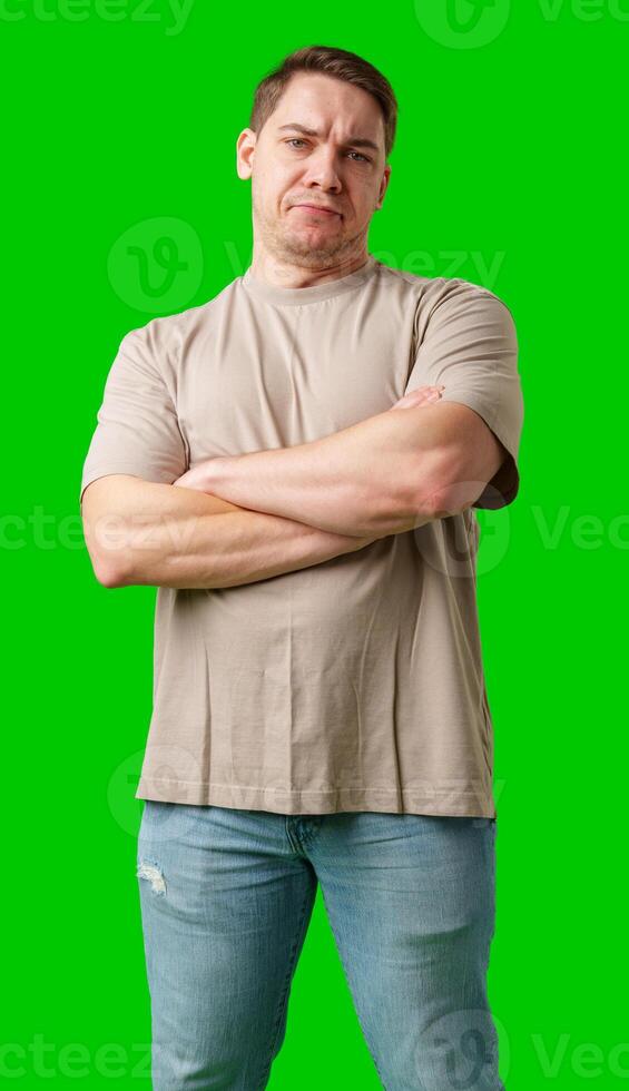 Young man making a disgusted expression while standing against a bright green background photo
