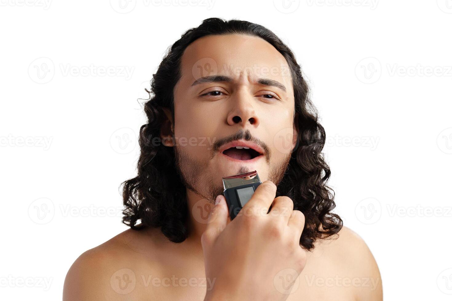 A young man with curly hair grooming his beard using an electric trimmer photo