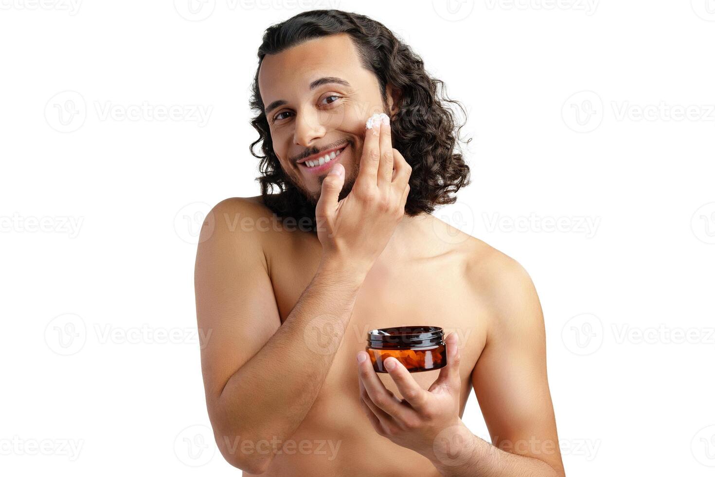 A young man applying skincare cream on his face with a focused expression, demonstrating personal grooming at home photo