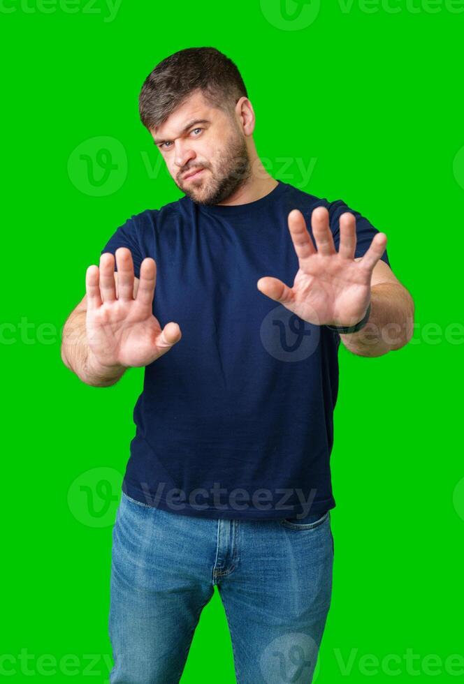 A man with a serious expression holds up both hands in a stopping gesture against a bright green background photo