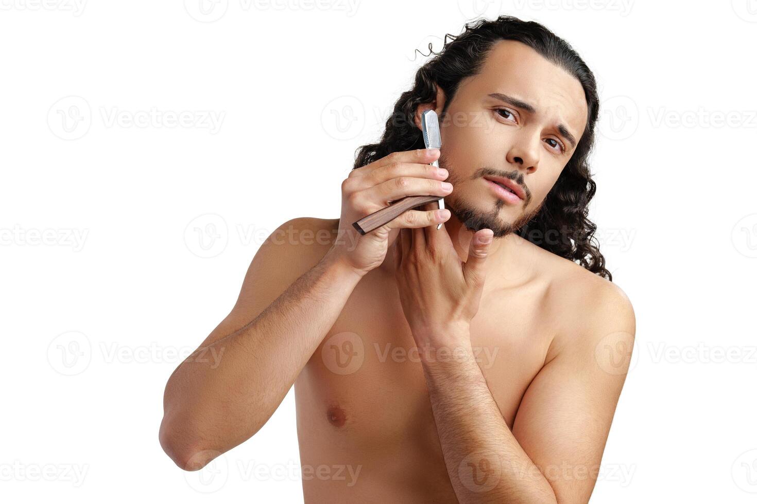 A man with curly hair grooming his beard in a well-lit space while using a straight razor photo