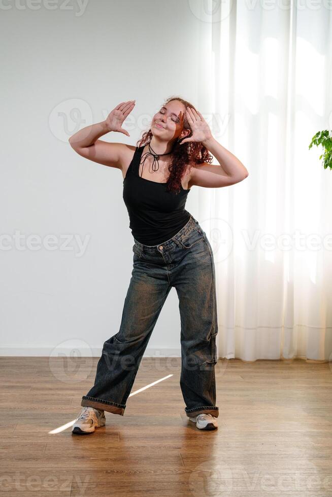 A young woman dances in a studio with a bright, natural light shining through the window behind her photo