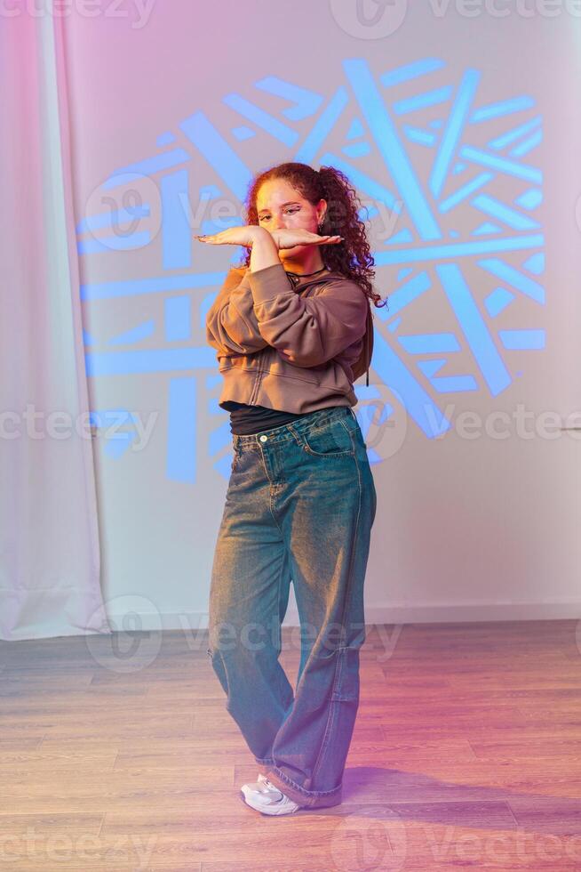 A young woman strikes a pose during a dance practice session in a studio with colorful lights photo