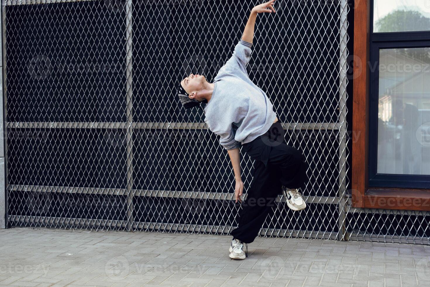 A dancer performs a move in front of a chain-link fence on a city street photo