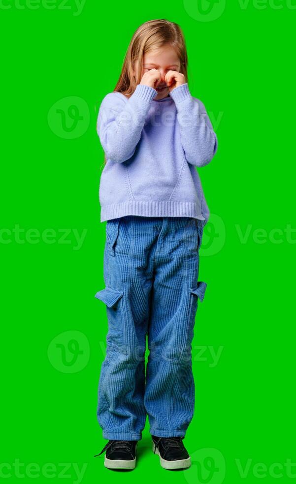 A young girl in a cozy sweater and blue cargo pants expressing emotion with a bright green background photo