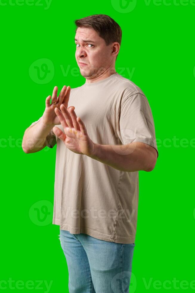 A man with a neutral expression gestures defensively against a bright green background photo