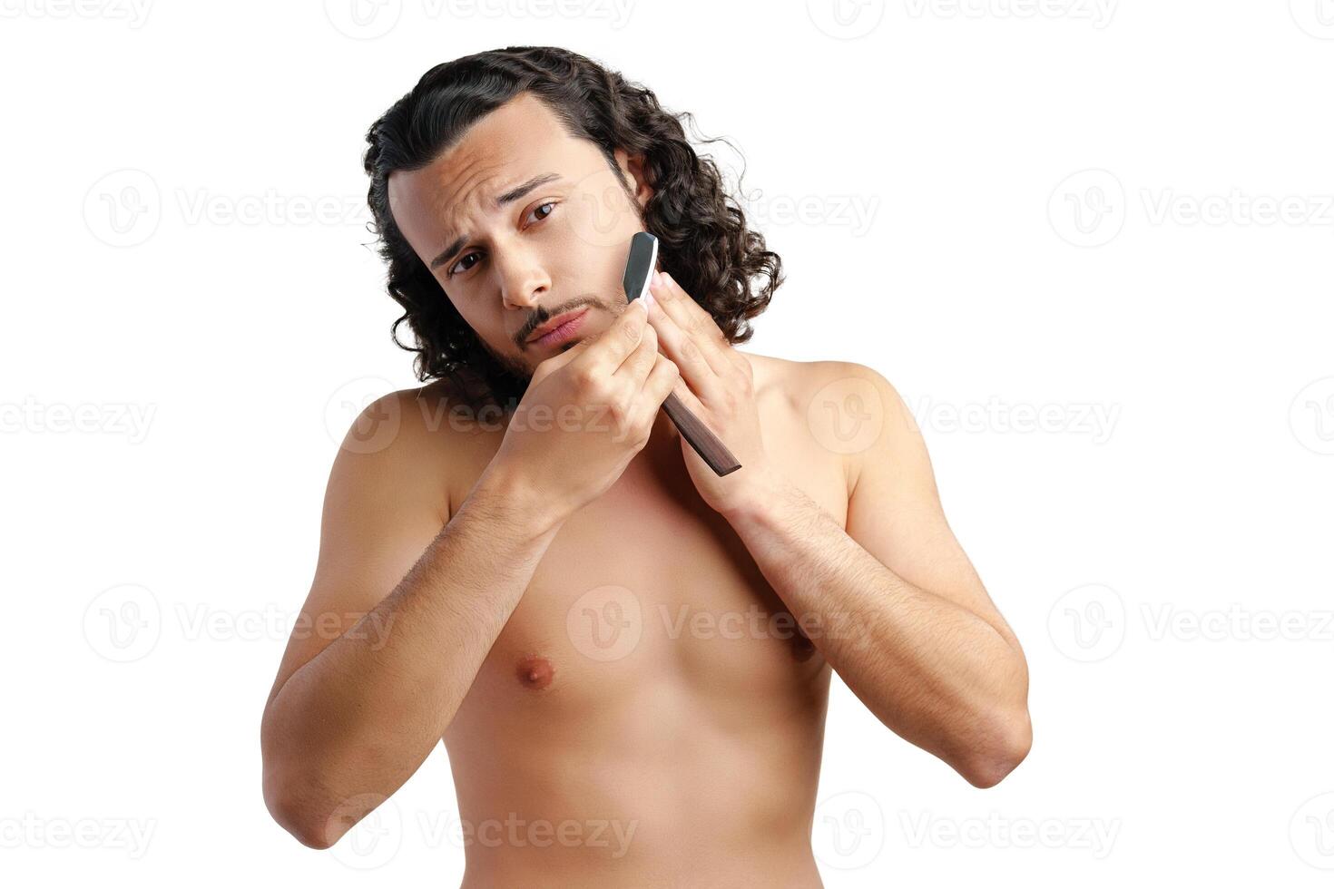 A man with curly hair grooming his beard in a well-lit space while using a straight razor photo