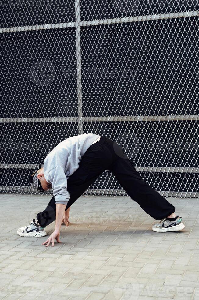 A person stretches in front of a chain link fence, reaching their hands down to touch the pavement photo