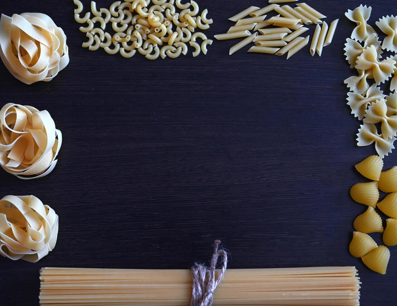 A close-up shot of a variety of pasta, including spaghetti, macaroni, and fettuccine, laid out on a burlap table runner. photo