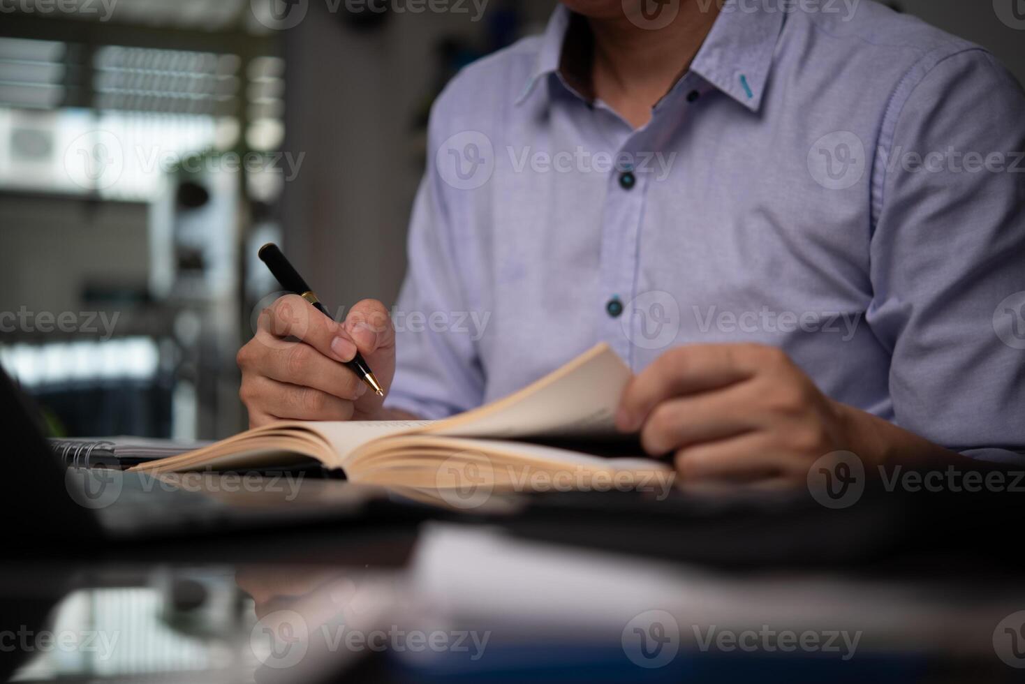 A man is writing in a book while sitting at a desk photo