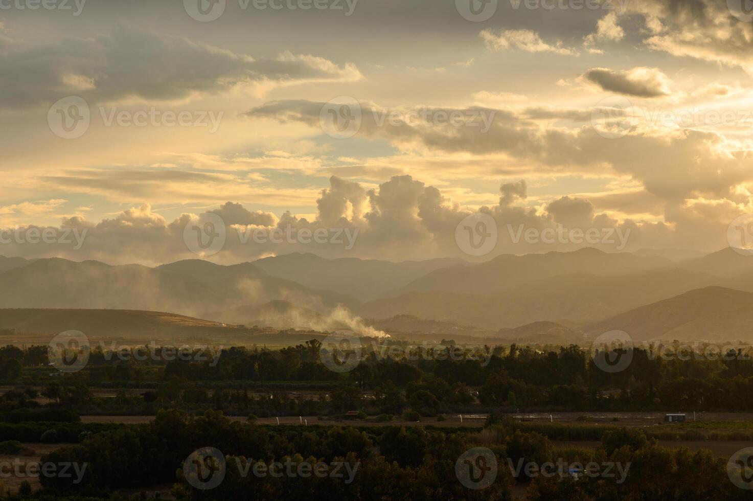 Majestic sunset over rolling hills with clouds and smoke in the distance photo