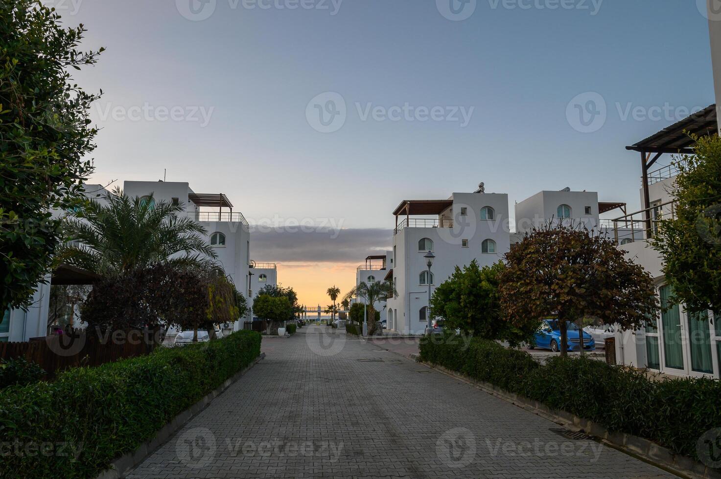 Serene coastal pathway lined with white buildings and greenery at sunset, inviting relaxation and exploration photo