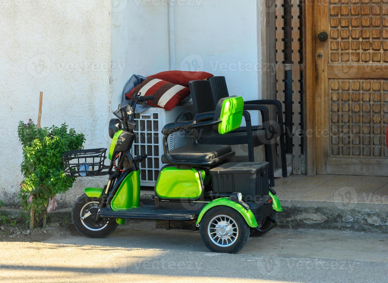 Colorful electric scooter leaning against a rustic door in a sunlit street setting. photo