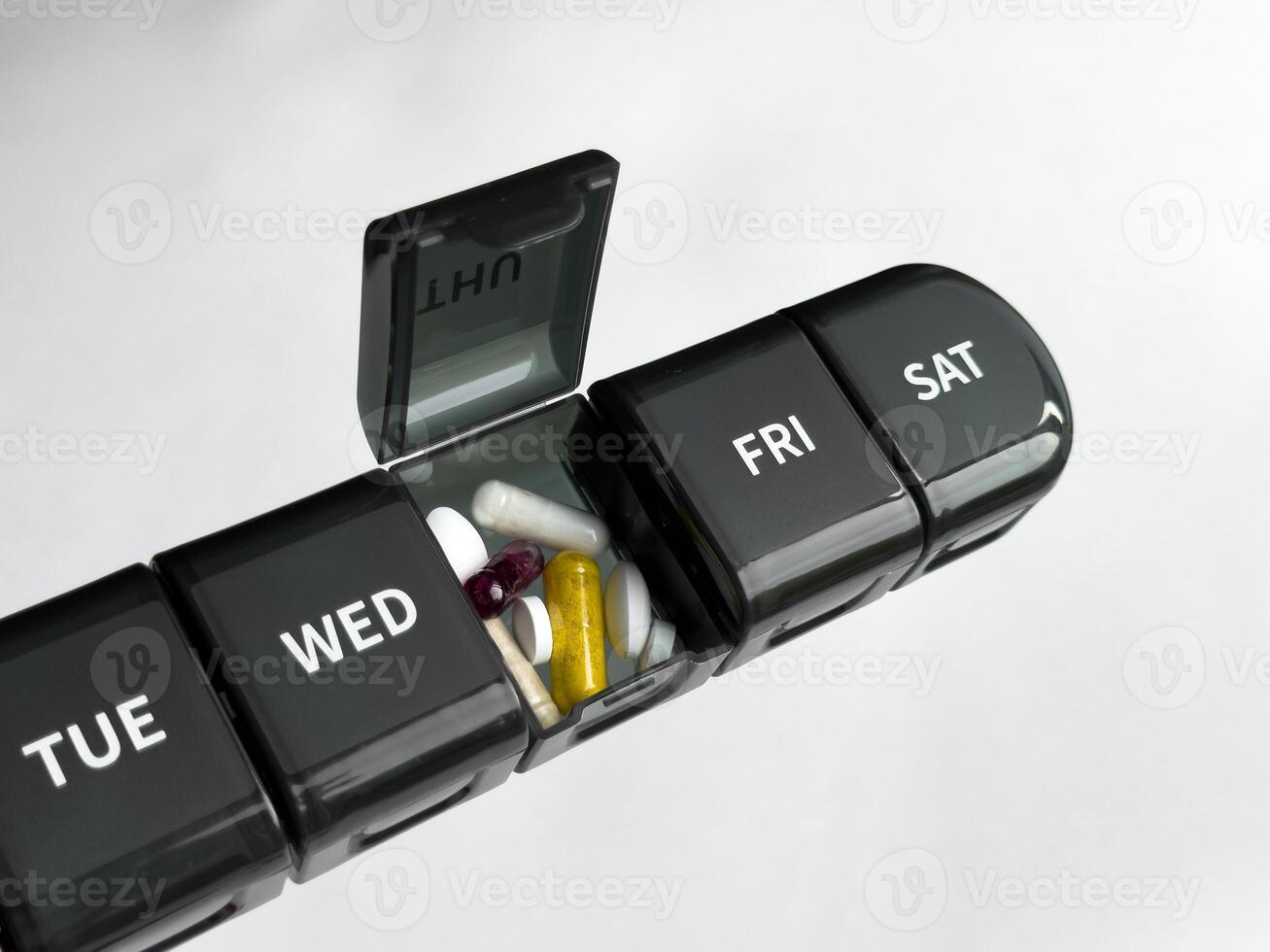 Weekly pill organizer with various capsules and tablets on neutral background photo