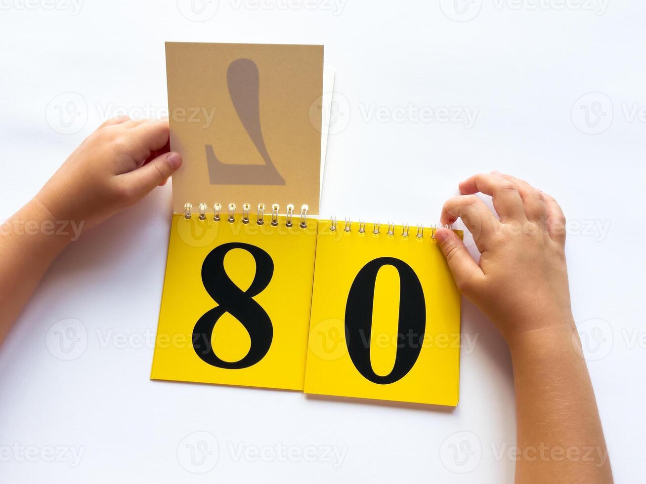 Childs hands flip through yellow pages with numbers. Displaying number 80 on white background photo