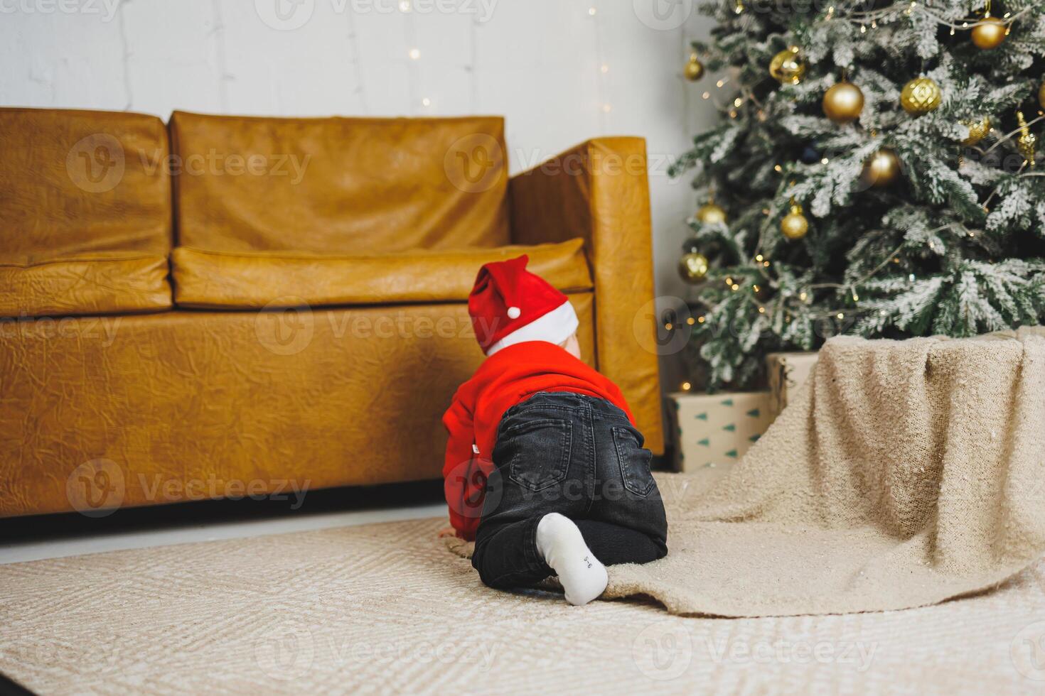 A little boy 1 year old sits in a basket against the background of a Christmas tree. A child in a red New Year's wind near the Christmas tree photo