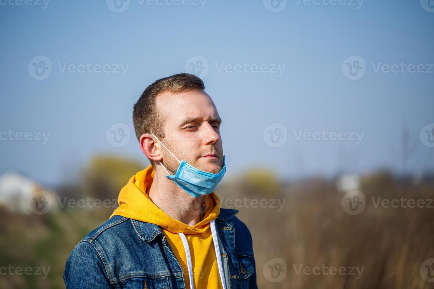 Close up portrait of a man outdoor in a surgical mask with rubber ear straps. Typical three-layer surgical mask for covering the mouth and nose. Bacteria mask procedure. Protection concept. photo