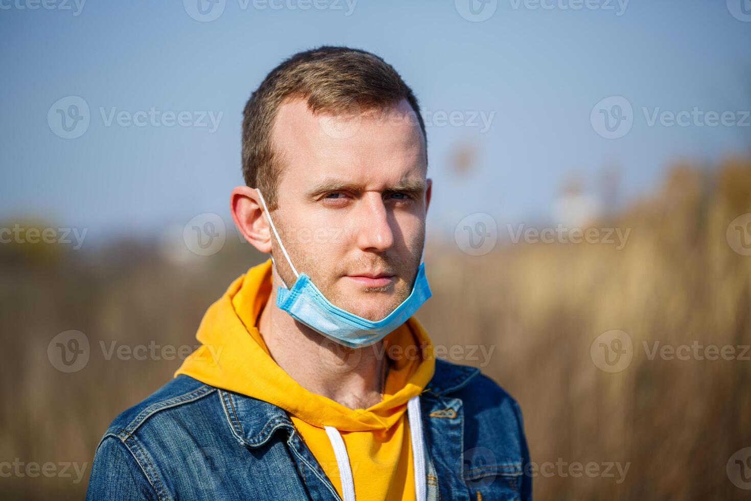 Close up portrait of a man outdoor in a surgical mask with rubber ear straps. Typical three-layer surgical mask for covering the mouth and nose. Bacteria mask procedure. Protection concept. photo