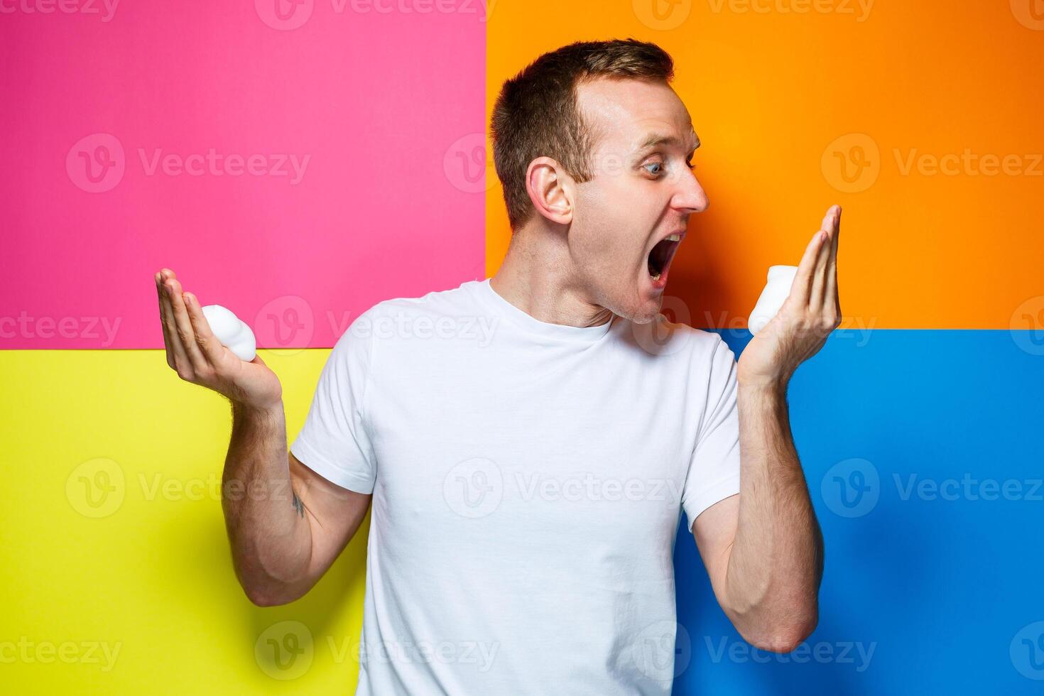 portrait of a young cheerful guy on a multi-colored background, dressed in a white T-shirt, poured hair foam in his hands, creates a fashionable hairstyle photo