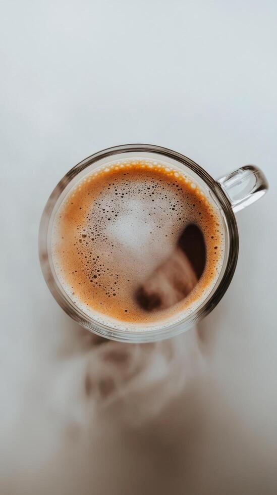 Hot coffee in a clear mug with steam rising on a white table surface photo