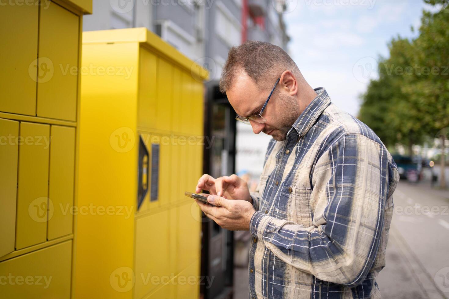 Man interacts with his smartphone near a bright yellow locker on a sunny day photo