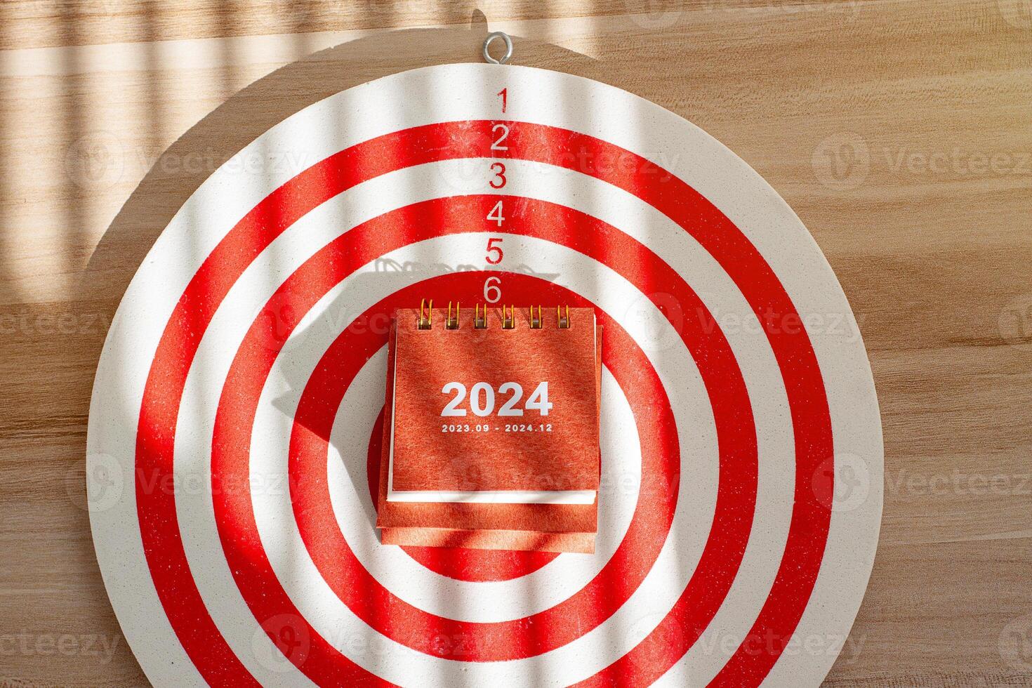 close up 2024 small calendar on dartboard, red dart arrow hitting photo