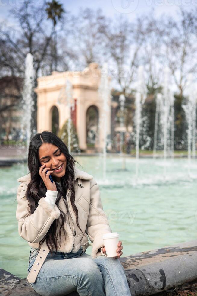 vertical Latin girl talking on the cell phone and having a coffee photo