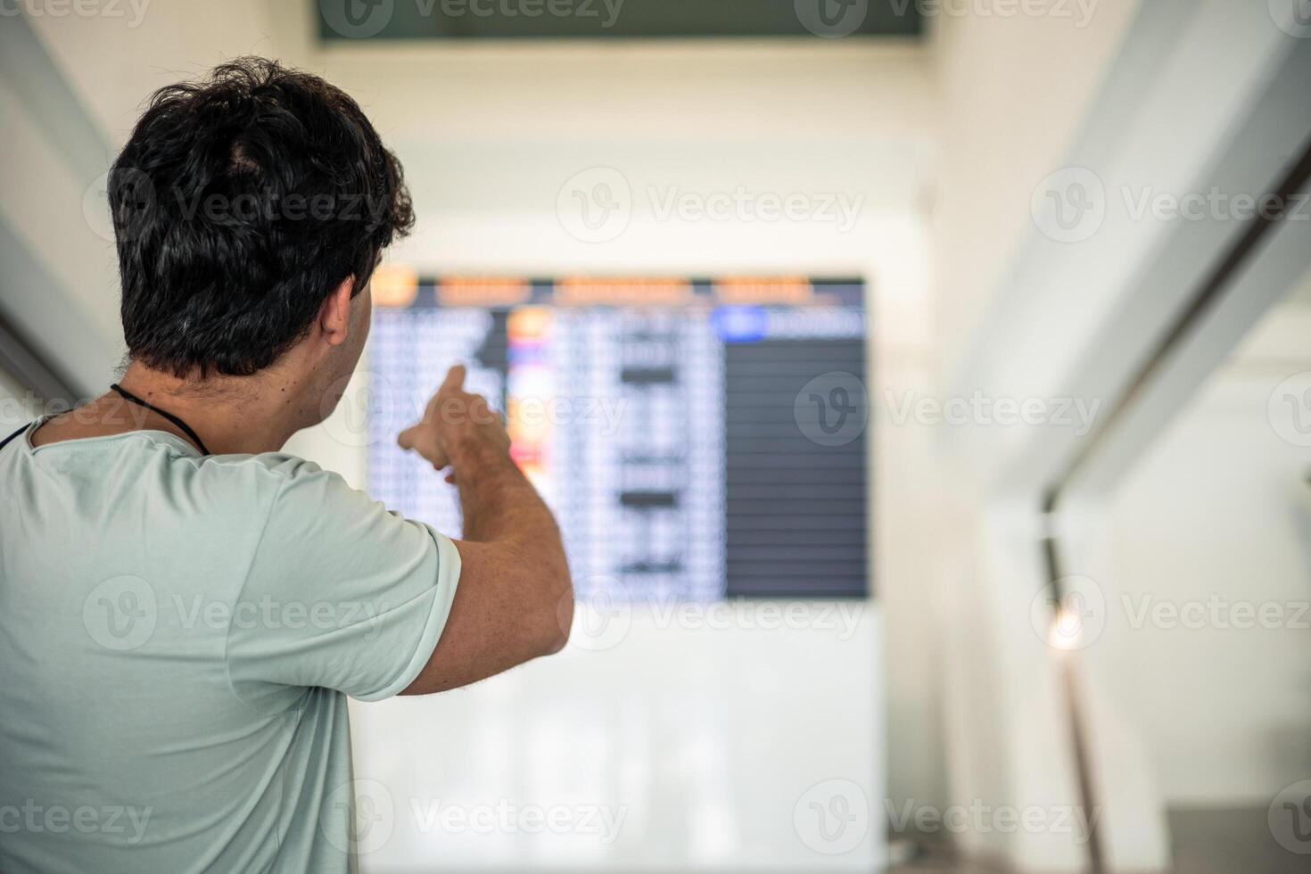 Traveler man photographed from behind pointing to the terminal timetable photo