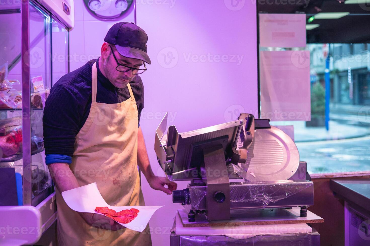 butcher Holding Freshly Sliced Marinated Pork Loin Next to Meat Slicing Machine photo