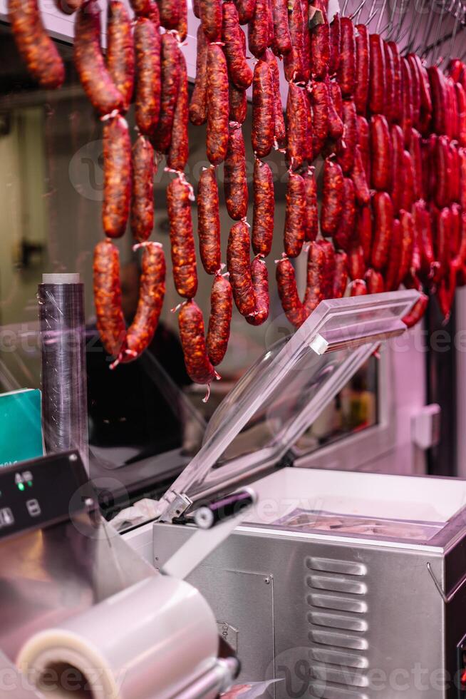 vertical portrait Vacuum Sealing Machine in Butcher Shop with Chorizos Hanging in Foreground photo