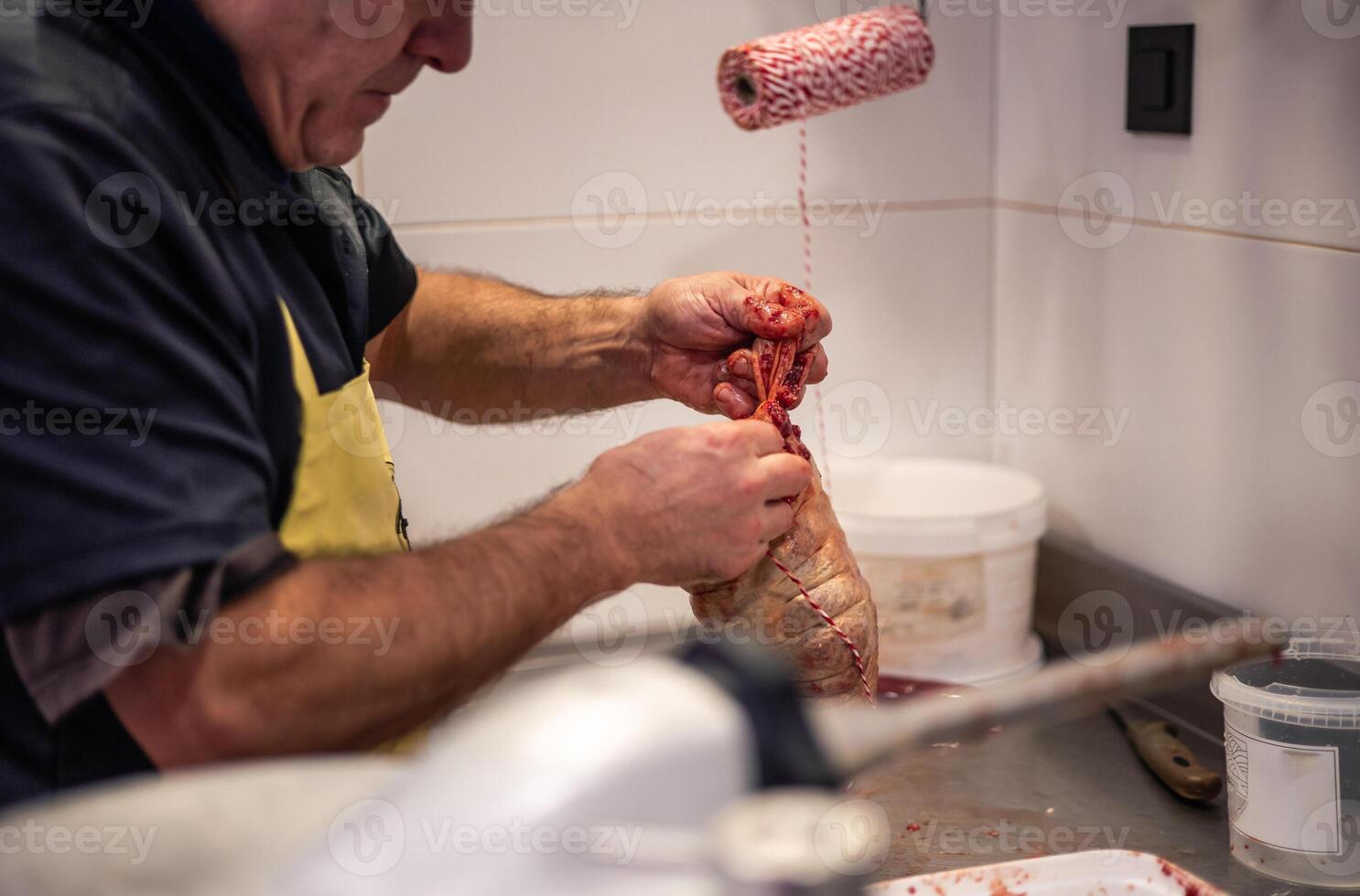 Closeup of Butcher's Blood-Stained Hands Tying Stuffed Chicken with Rope photo