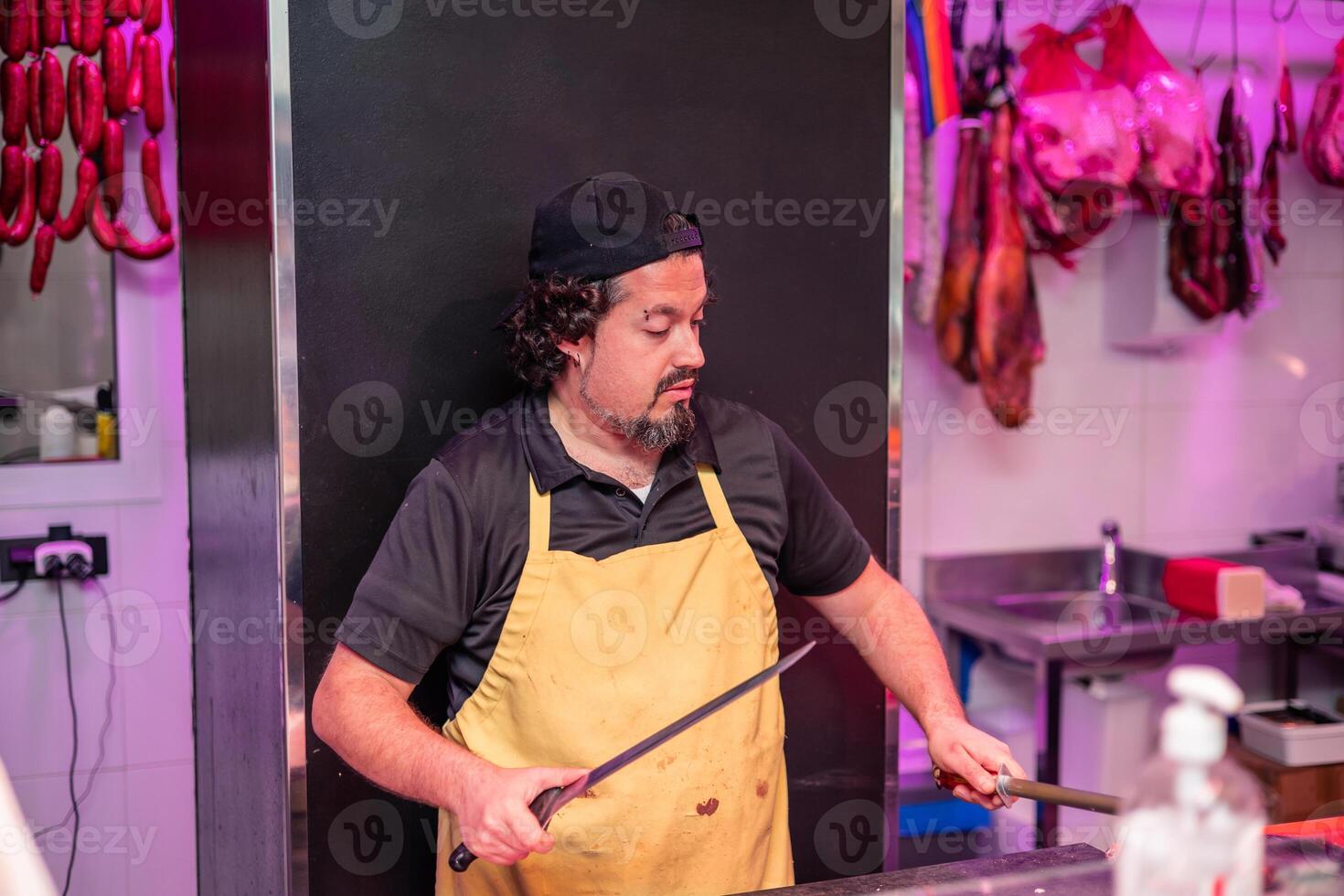 Butcher Sharpening Knife Behind Butcher Shop Counter in Yellow Apron photo