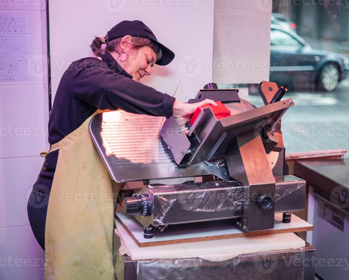Focused Female Butcher Cutting Beef Loin with Electric Slicer in Butcher Shop photo