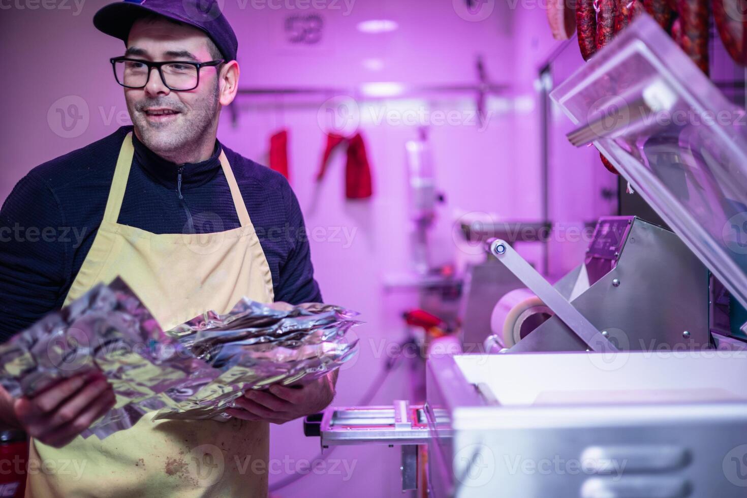 Smiling Butcher Holding Packaged Meat Next to Packaging Machine copyspace photo