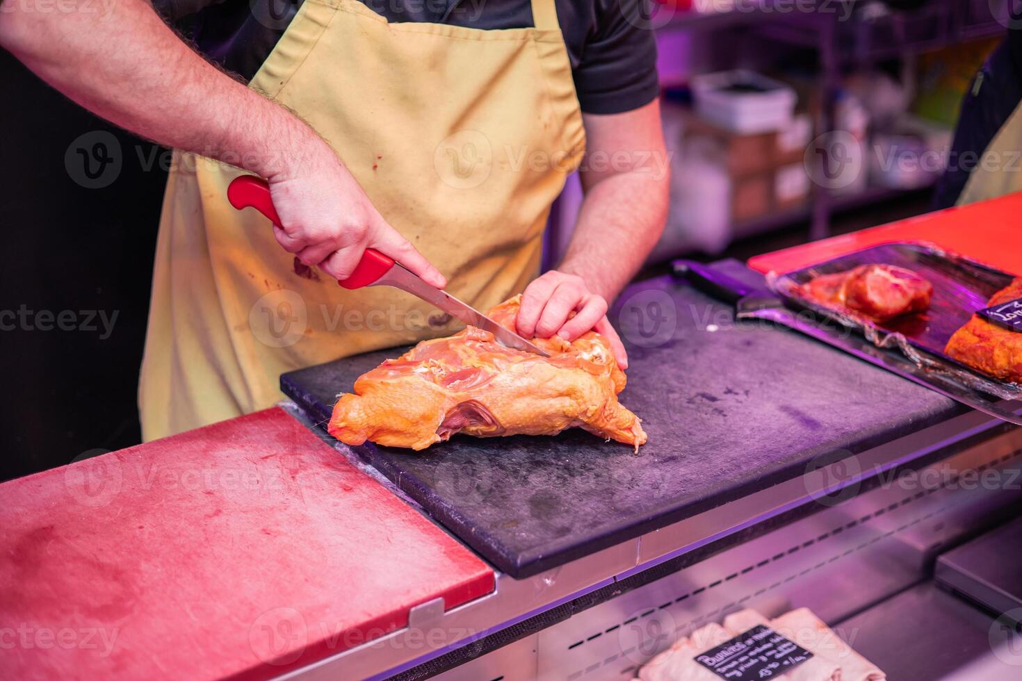 Closeup of Butcher's Hands in Yellow Apron Cutting Chicken for Customer at Butcher Shop Counter photo