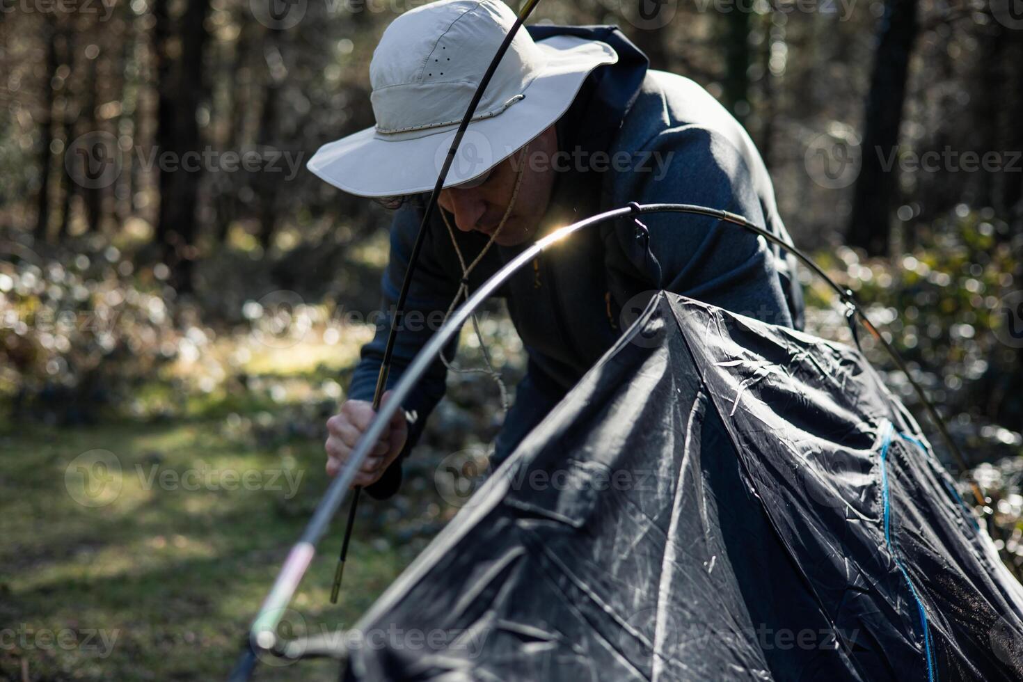 closeup Man with hat setting up tent in forest at sunset photo