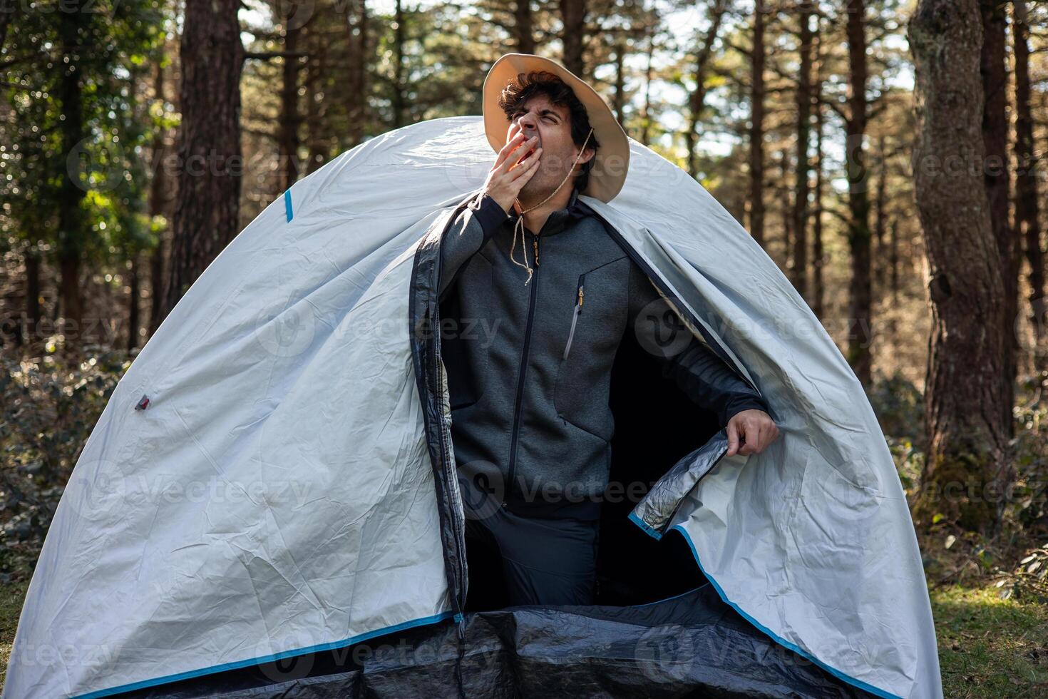 Camper Yawning at Tent Door on Summer Morning in Forest photo