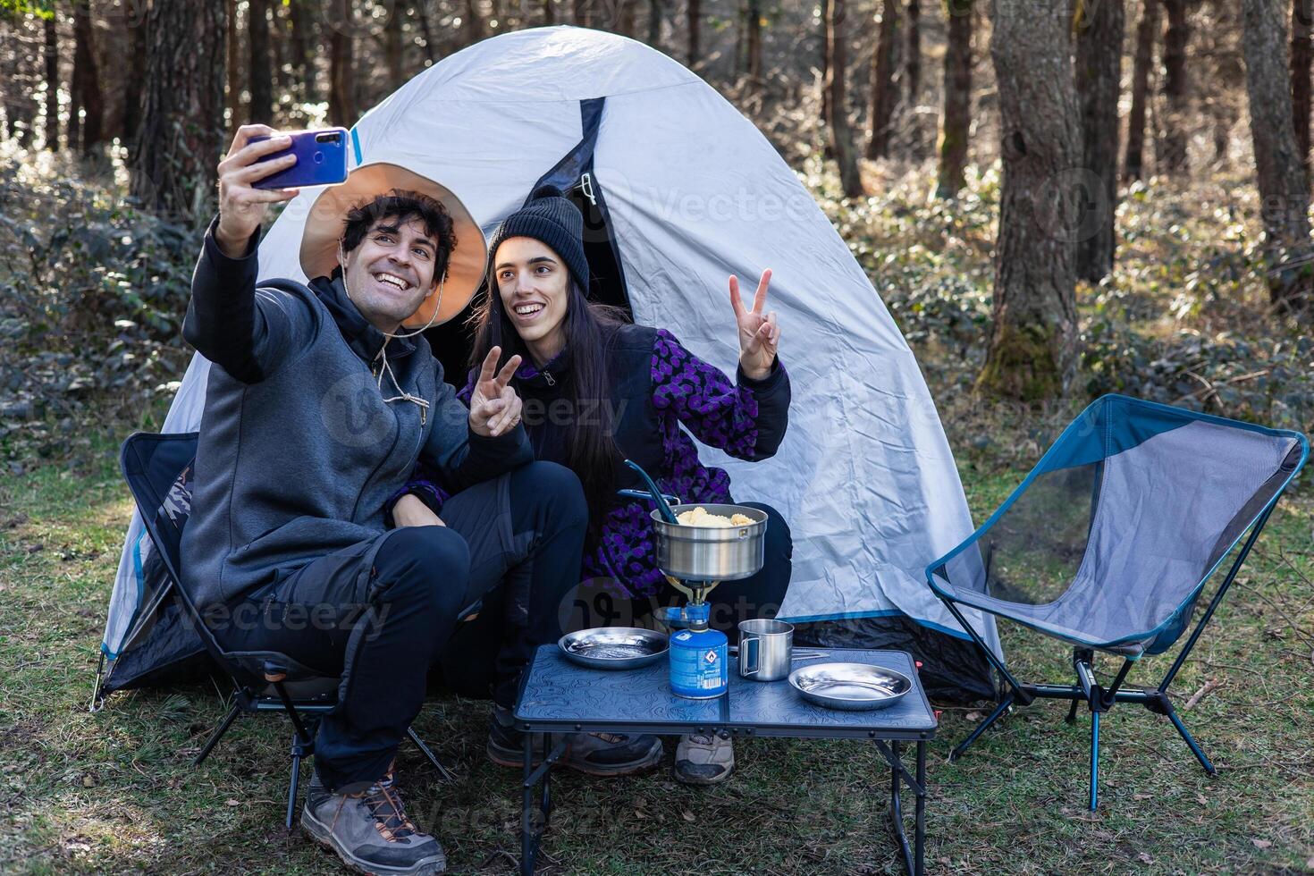 Multicultural campers taking selfie with smartphone at summer sunset campsite photo
