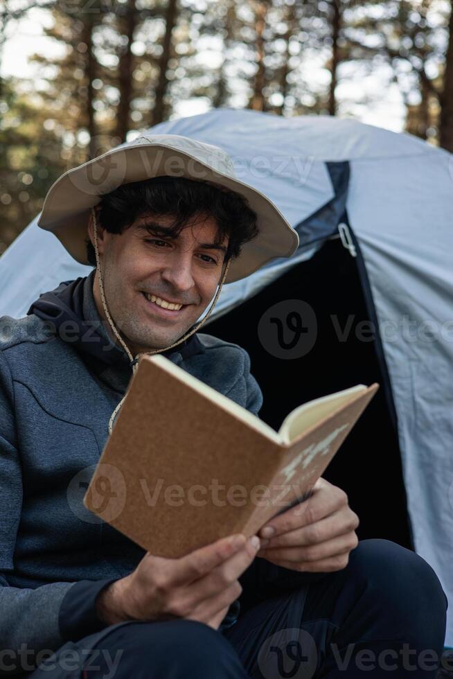 vertical portrait closeup Smiling young camper reading book in wildness campsite photo