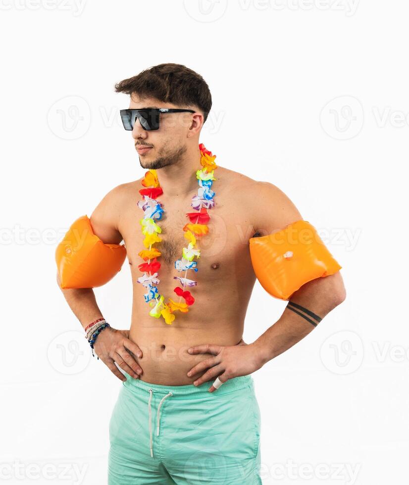 Young man in swim trunks with sunglasses, flower necklace, and arm floats on white background photo