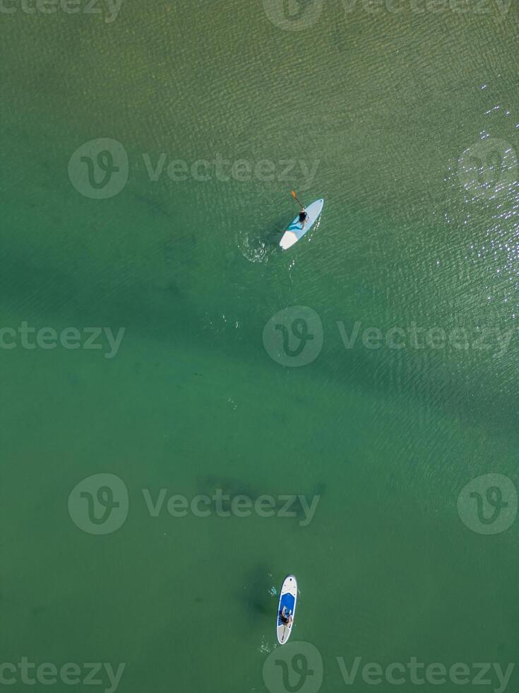 vertical Multicultural couple paddleboarding on a river on a summer day, top view photo