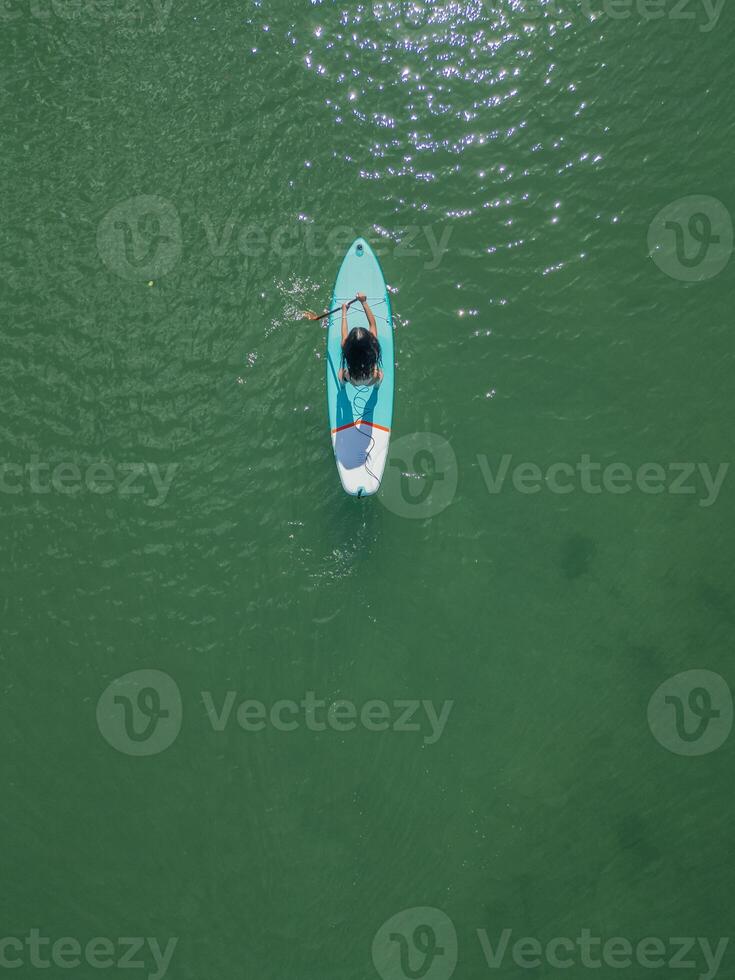 vertical cenital copyspace above view hispanic girl paddleboarding with board in the sea photo