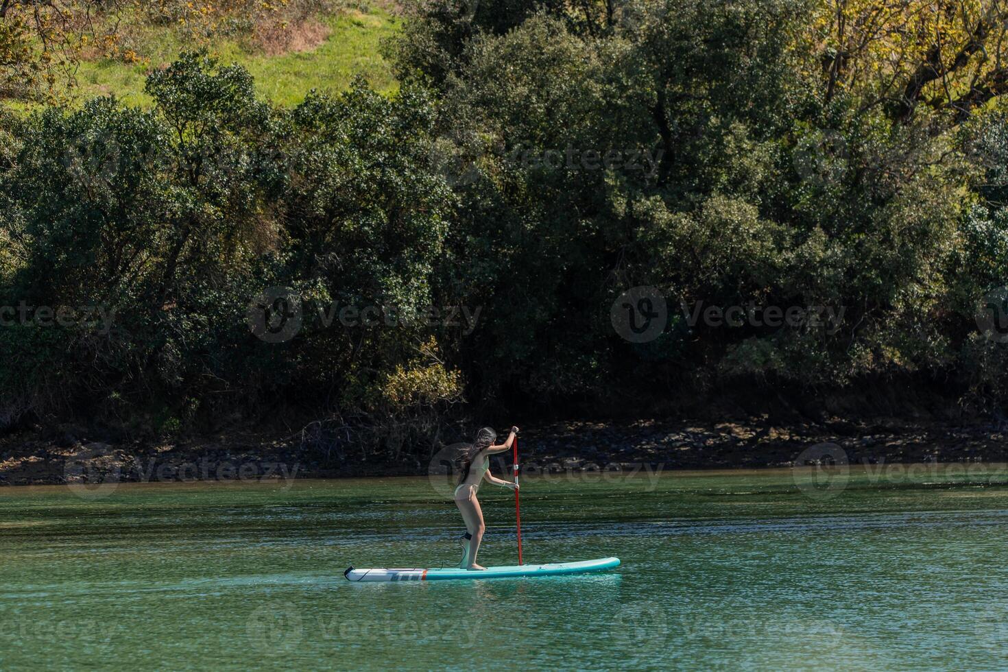Multicultural Woman in bikini Paddleboarding on River side view photo