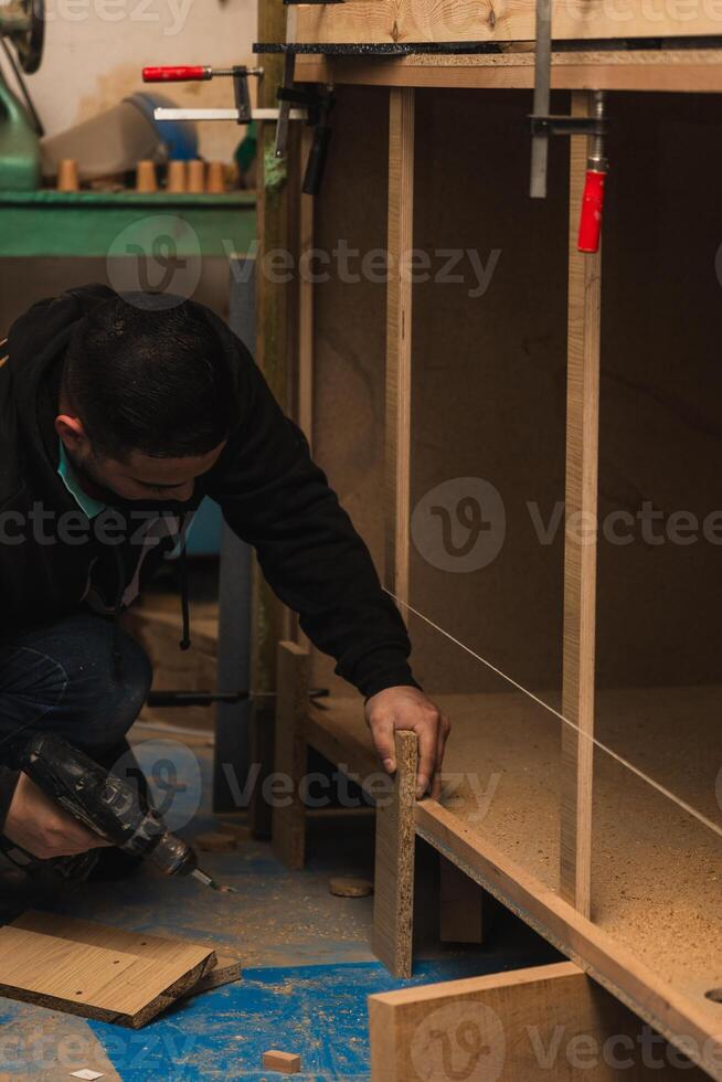 Latin Carpenter Using Drill to Repair Furniture in Carpentry Workshop photo