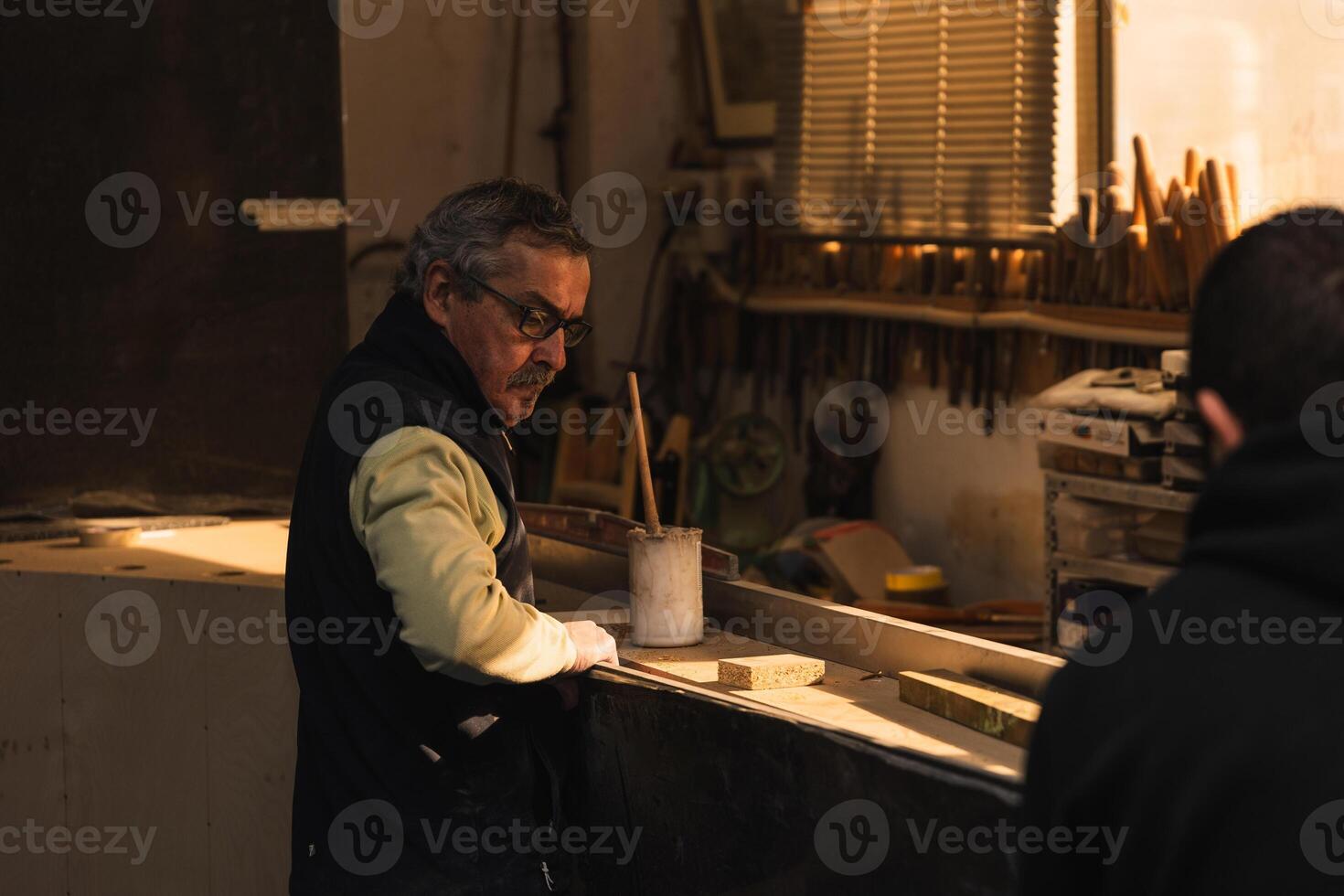 Elderly Carpenter and Latin Assistant Selecting Wood for Varnishing in Carpenter Workshop photo
