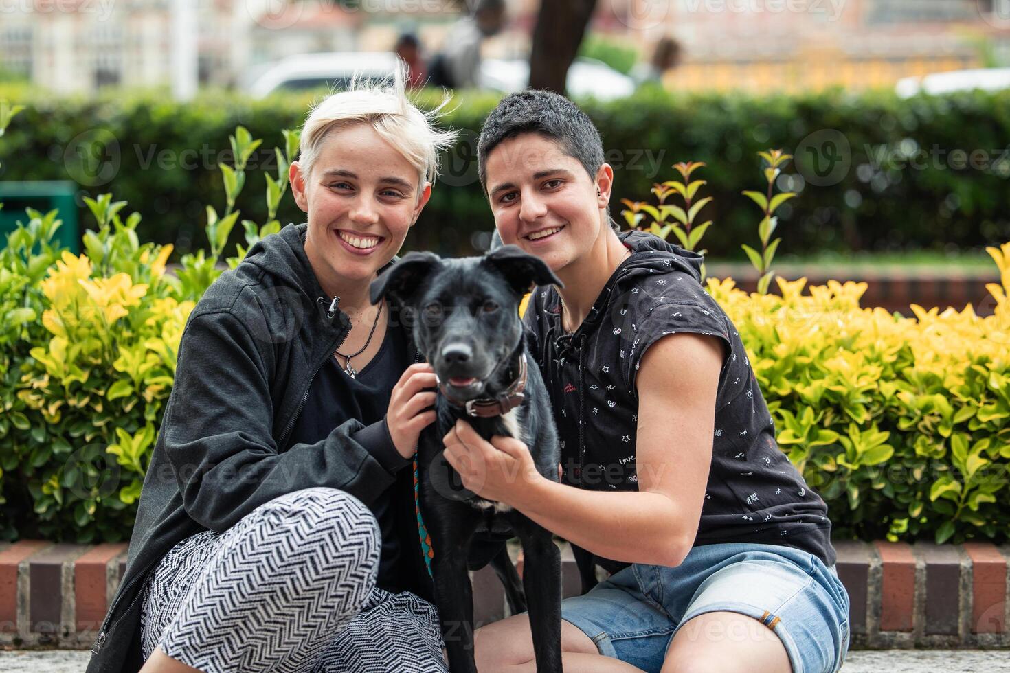 Lesbian couple and their dog posing for a photo in the garden, looking at the camera