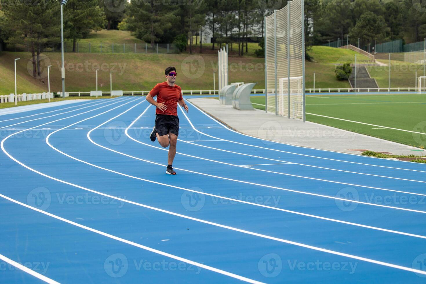Wide Shot of Male Runner with Sunglasses Training on Blue Athletic Track photo